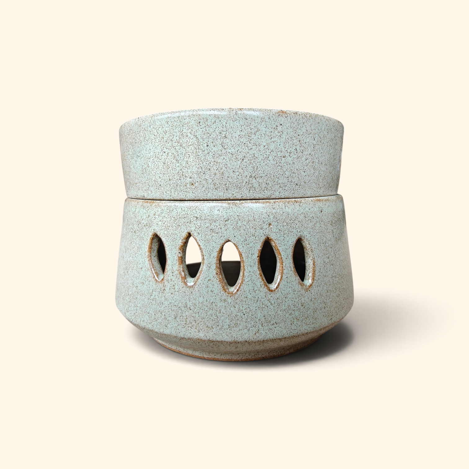 A small ceramic diffuser with a speckled light blue-green glaze and five oval cutouts on the front, shown on a plain beige background.